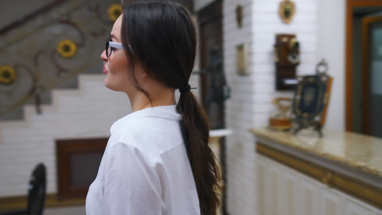 Elegant woman at reception desk in hotel. Young lady in white blouse and red skirt taking the key from the room and settling in hotel. Rear view.
