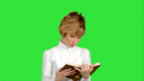 concentrated young business woman holding and reading book on a green screen, chroma key