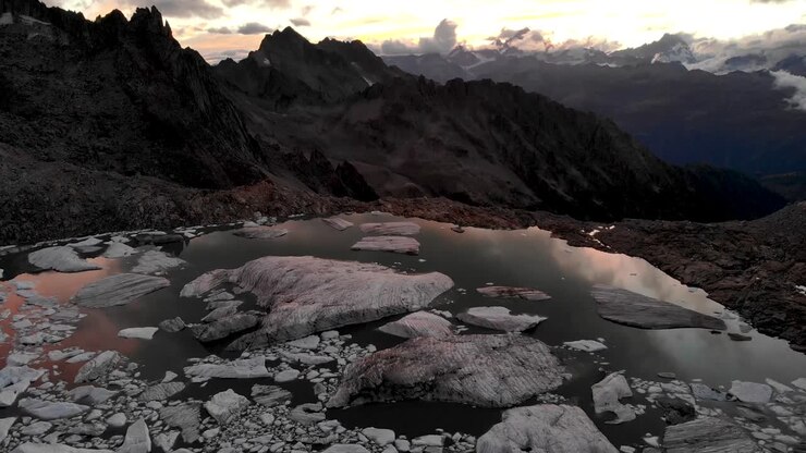Aerial view of a glacier lake full of melted icebergs in remote parts of the Swiss Alps during sunset with pan down