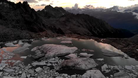 Vista-Aérea-De-Un-Lago-Glaciar-Lleno-De-Icebergs-Derretidos-En-Partes-Remotas-De-Los-Alpes-Suizos-Durante-La-Puesta-De-Sol-Con-Pan-Hacia-Abajo