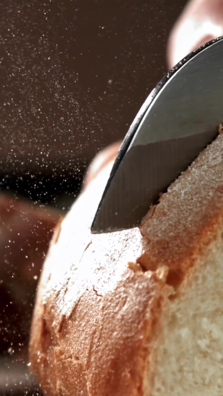 Close-up of a Knife Slicing Freshly Baked Bread with Crumbs Falling