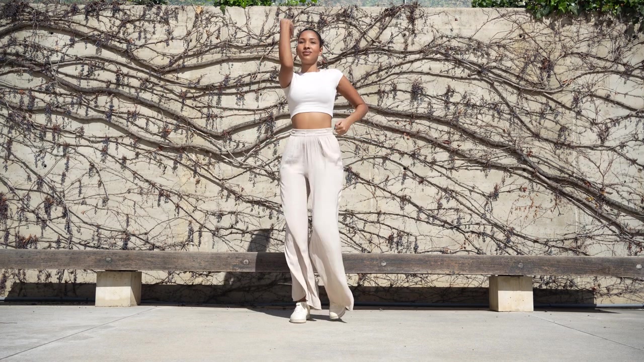 A stylish woman gracefully posing in an urban setting with a colorful artistic wall behind her