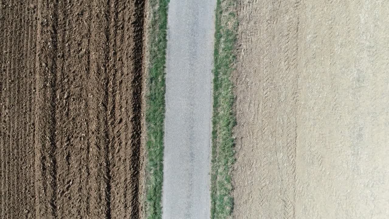 Aerial drone shot of a pebbled road in between farm fields