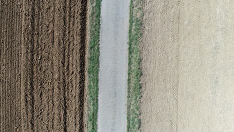 aerial drone shot of a pebbled road in between farm fields