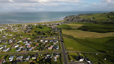 Living-homes-of-coastal-New-Zealand-town-surrounded-with-agriculture-fields,-aerial