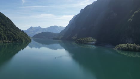 Wasser,-Eingebettet-Zwischen-Majestätischen-Bergen,-Erstreckt-Sich-über-Den-Hintergrund.-Ihre-Gipfel-Sind-Mit-Einer-Mischung-Aus-Nebel-Und-Wolken-Bedeckt.-Das-Wasser-Spiegelt-Den-Bewölkten-Himmel-über-üppigen-Grünen-Bäumen-Wider,-Ein-Boot-Prahlt-Herum