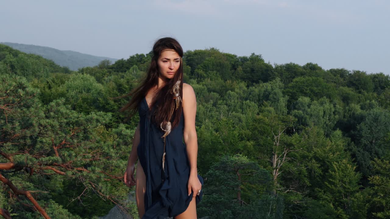 hermosa mujer medieval salvaje en vestido azul con plumas en el cabello se encuentra mirando al sol