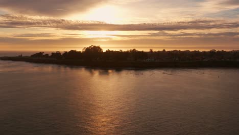 Panorámica-Hacia-La-Derecha,-Toma-Baja-De-Drones-Mirando-A-Docenas-De-Surfistas-Al-Atardecer