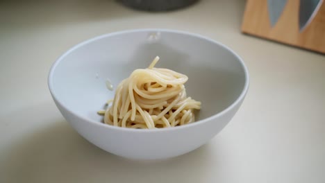 serving homemade spaghetti in a white bowl, kitchen interior, close-up