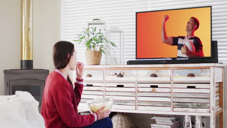 mujer caucásica viendo la televisión con un jugador de rugby caucásico con la pelota en la pantalla