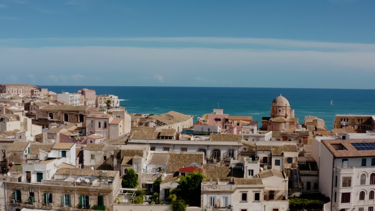 Drone shot flying sideways above historic buildings in the island of Ortigia, Syracuse. Medieval old town buildings from above with Mediterranean sea in the background. UNESCO world heritage site.