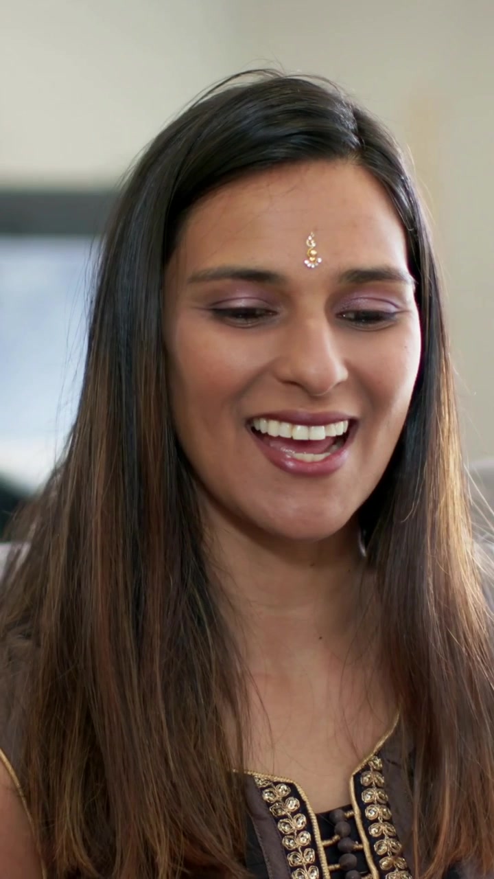 Vertikal video: Hör röst utanför bild, indisk kvinna ler, skrattar i soffa i kurta och bindi.