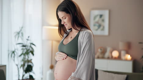 A pregnant woman holding her baby bump at home