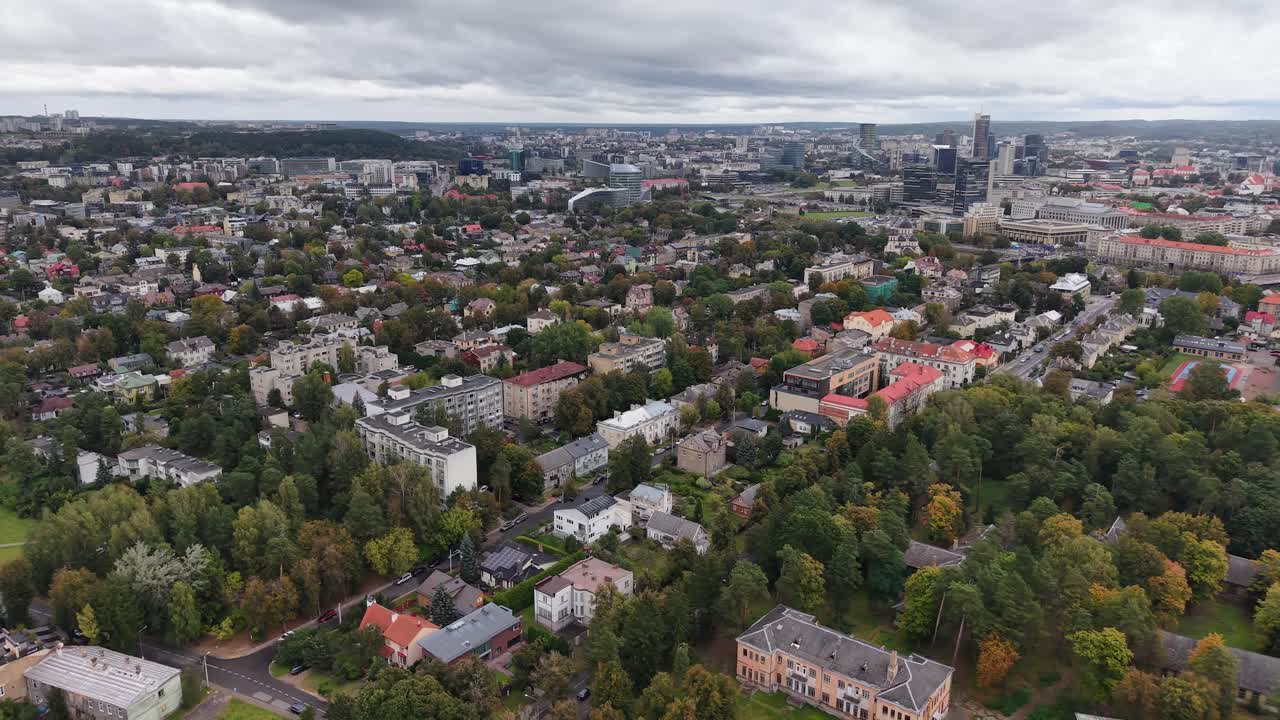 Ilmakuva, jossa lähestytään Vilnaa rakennusten, asuntojen ja puiden yllä