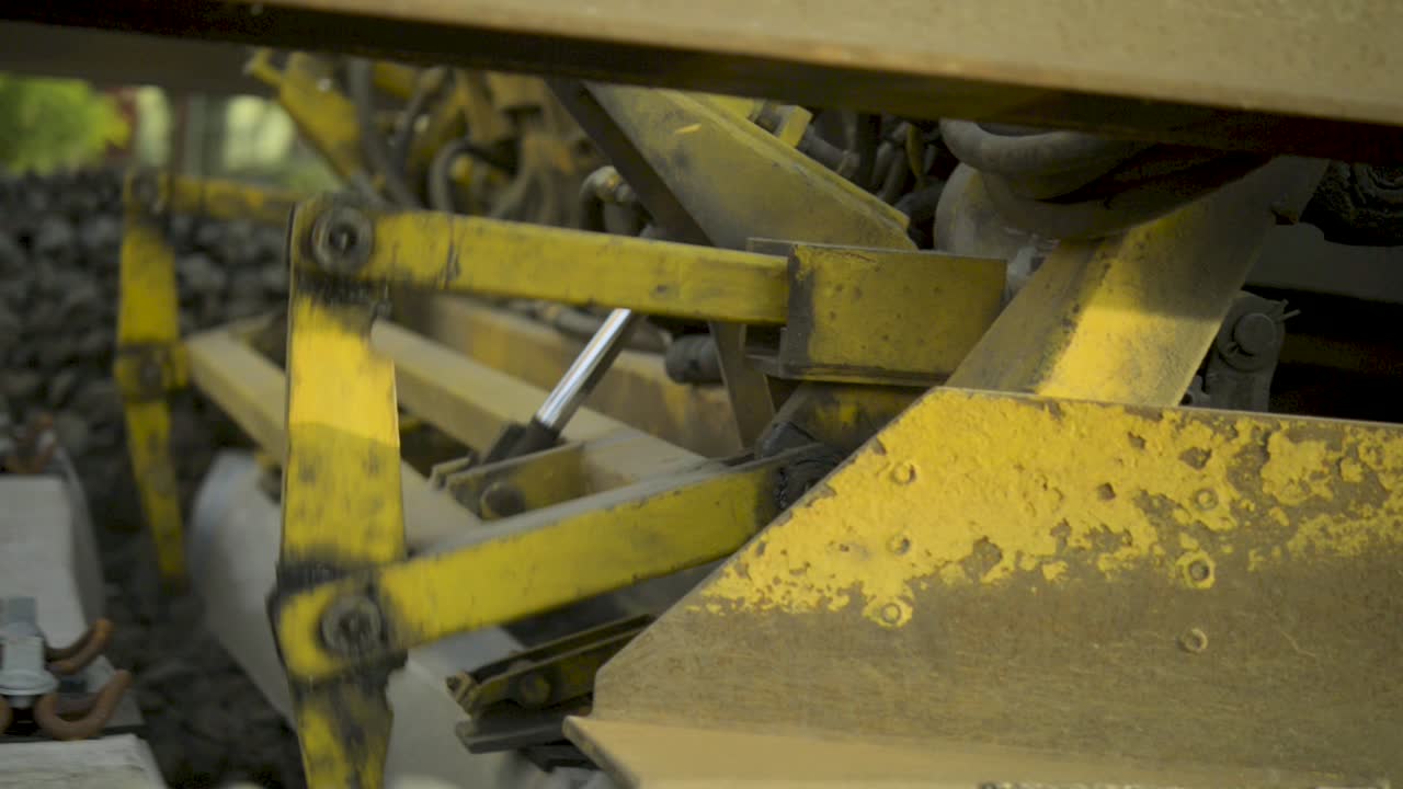 primer plano de una máquina de mantenimiento ferroviario amarilla con engranajes y mecanismos enfocados