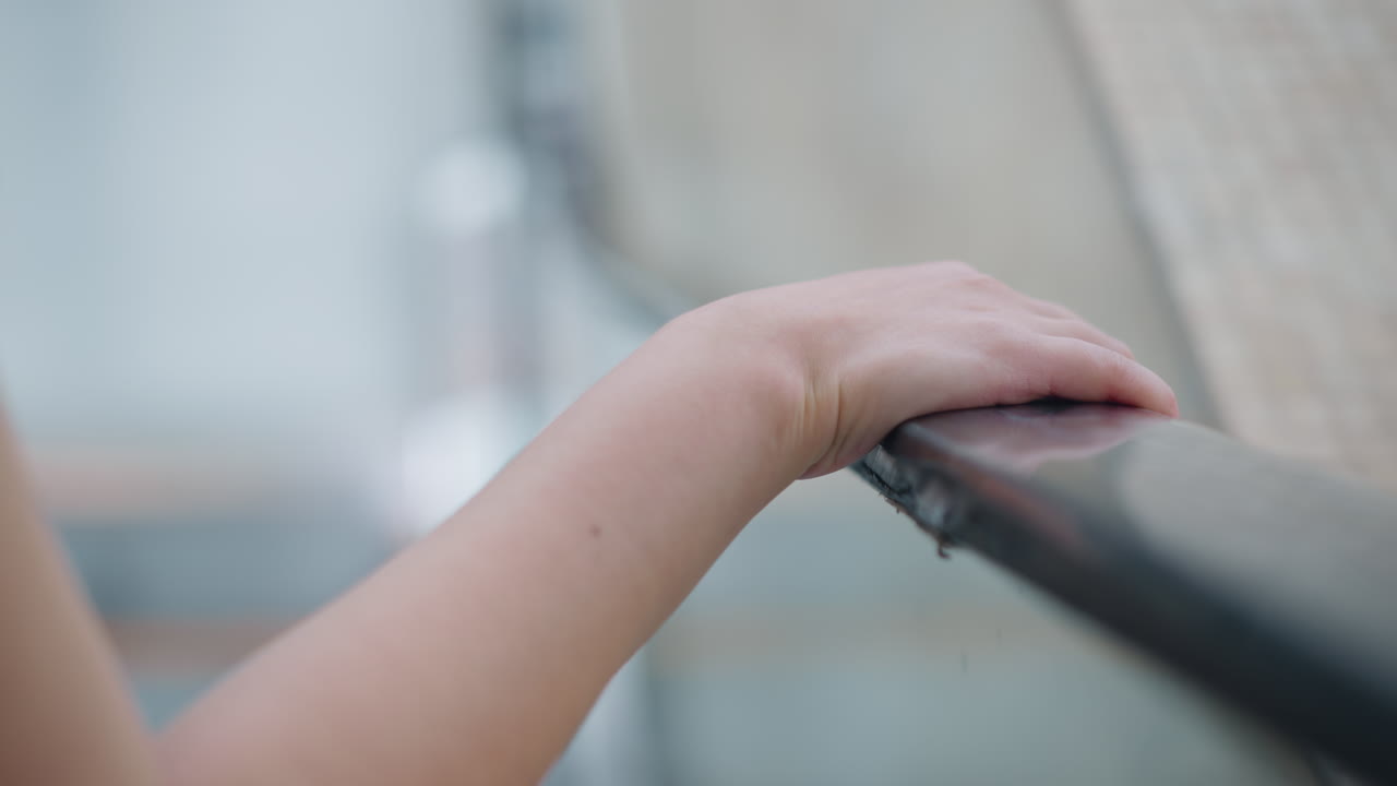 여성의 오른손이 에스컬레이터 레일에 누워있는 클로즈업, 부드러운 피부와 자연 손이 보이고, 현대적인 실내 환경에서 불분명한 인물이있는 흐릿한 배경