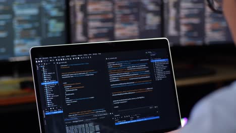 person coding on laptop with multiple monitors