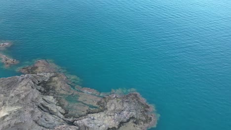 a perspective from above of a rocky cliff and the azure sea