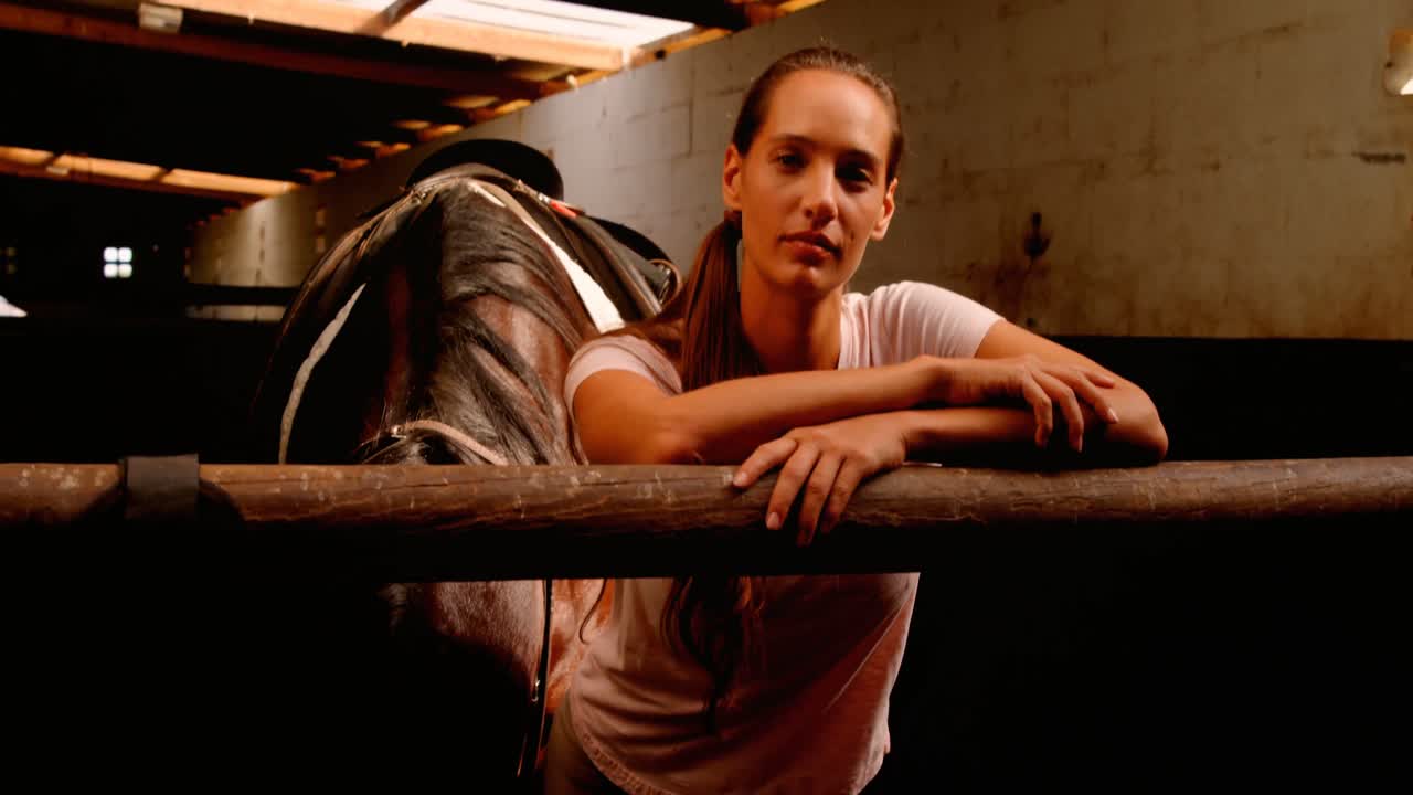 mujer de pie con el caballo en el establo 4k