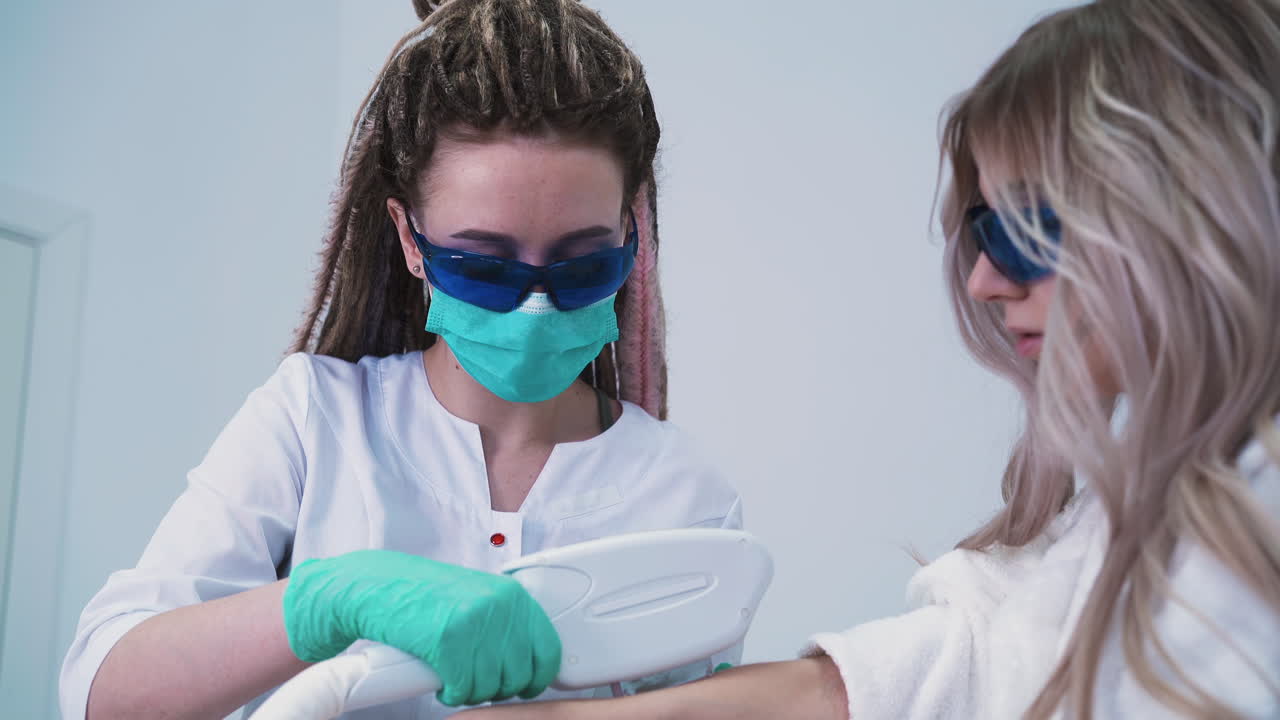 el cosmetólogo hace la depilación láser del brazo de la mujer en la clínica