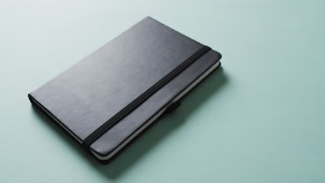 close up of closed black notebook with copy space on green background in slow motion