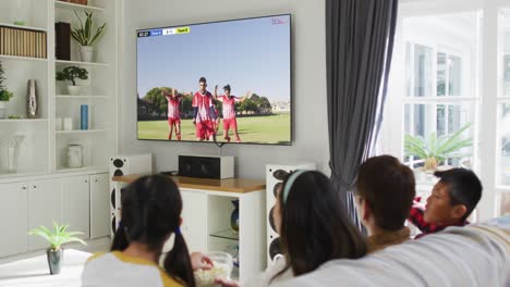 Video-Einer-Vielfältigen-Gruppe-Von-Kindern,-Die-Auf-Der-Couch-Sitzen-Und-Sich-Ein-Fußballspiel-Ansehen