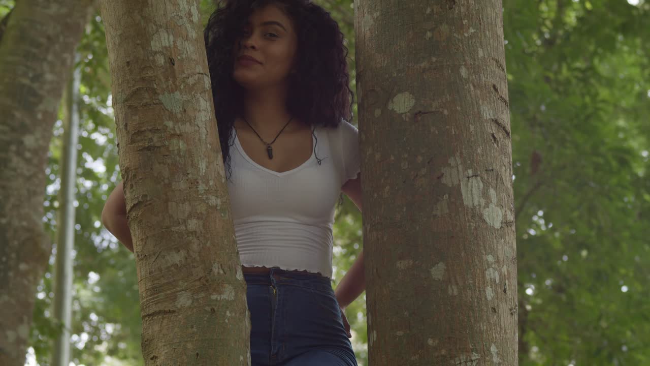 Belle femme latine souriante, debout entre deux troncs d'arbres.