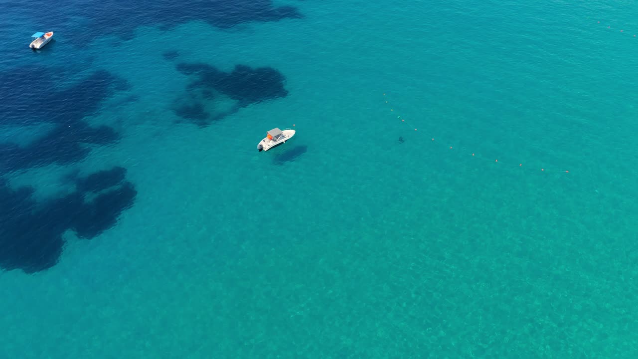 un barco flota en aguas cristalinas de color turquesa con manchas azules profundas, vistas desde arriba