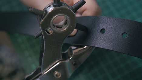 experienced worker makes holes in black leather belt