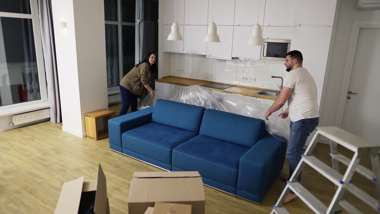Ægtepar fjerner dækkenet fra sofaen i deres nye lejlighed.