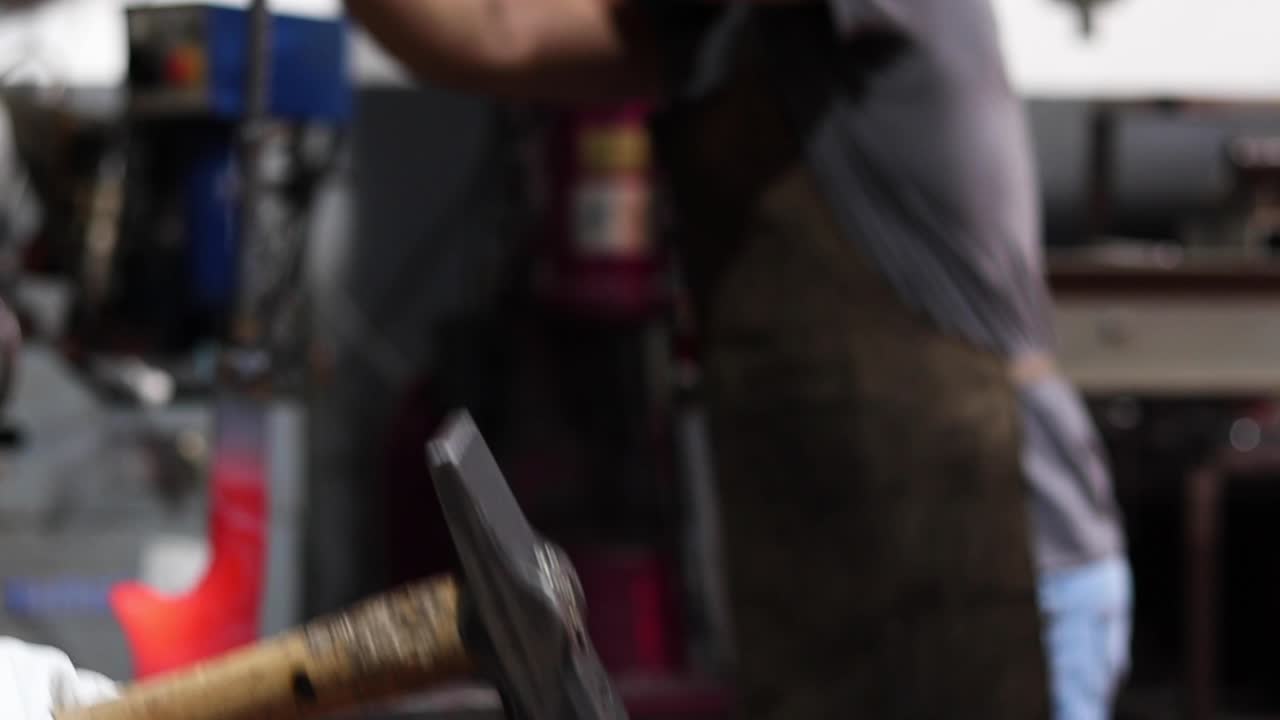 Blacksmiths forging hot metal with hammer in workshop