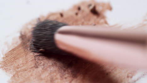 smudging a mixture of powder and liquid make-up foundation with a brush applicator on a white board palette