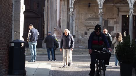 elderly man rides bicycle past people walking on cobblestone street in historic european city