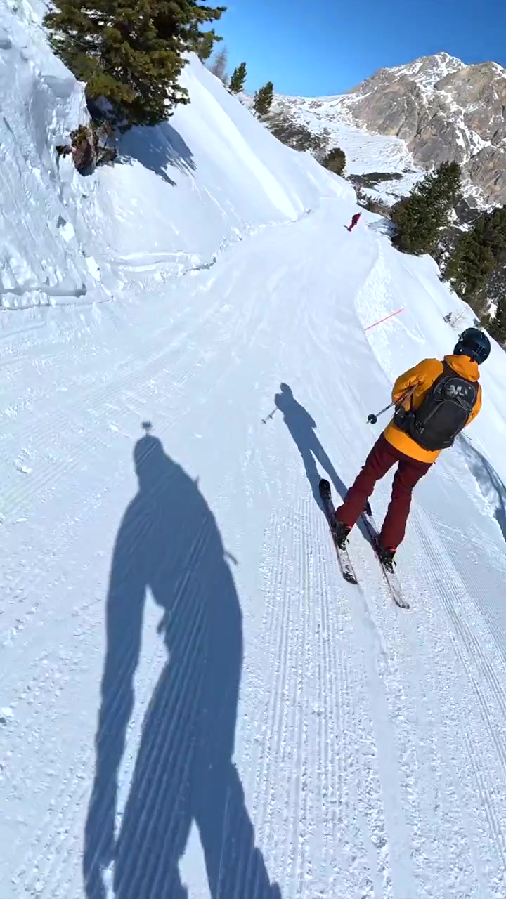 Snowboardista che segue uno sciatore su un pendio di montagna soleggiato