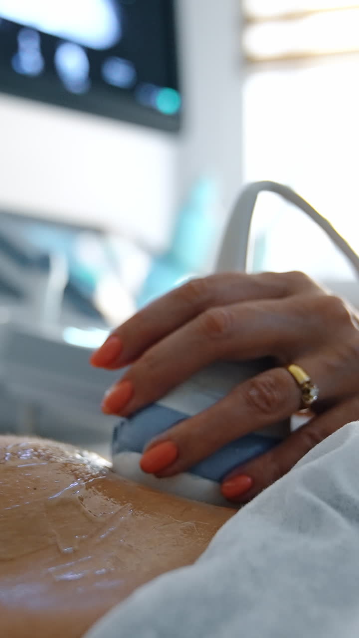 Medico che muove la sonda ecografica sul ventre cosparso di gel di una paziente incinta. Primo piano. Monitor della macchina sfocato sullo sfondo. Video verticale