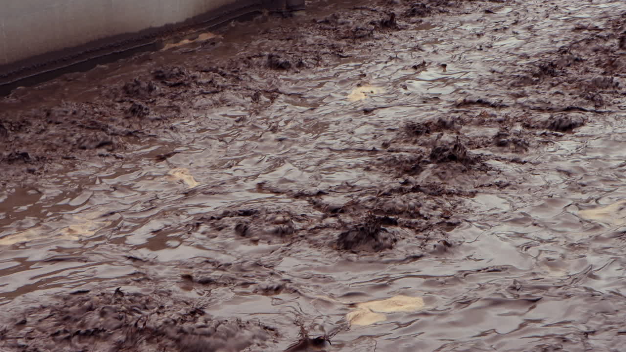 Chocolate-colored sewage churns in a wastewater treatment plant, captured in a smooth left-to-right pan, revealing industrial flow and processing in motion