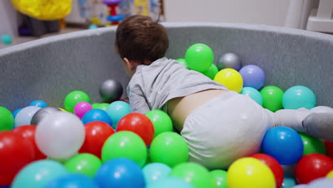 baby boy lying in the dry pool sits up. adorable child throws the ball ahead. blurred backdrop.