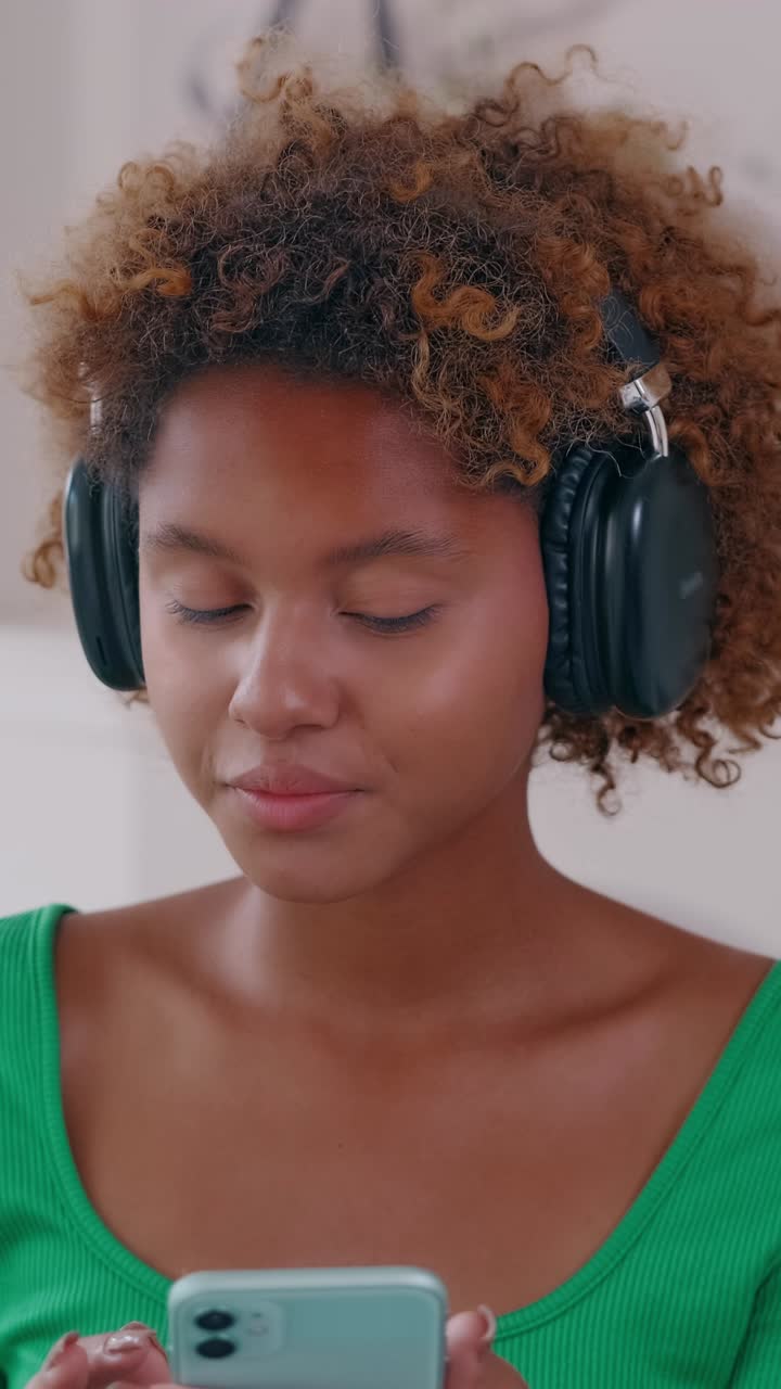 Young woman wearing headphones scrolling a smartphone in a bright interior