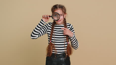 Child-girl-kid-holds-magnifying-glass-near-face-looking-at-camera-with-big-zoomed-eye,-analyzing