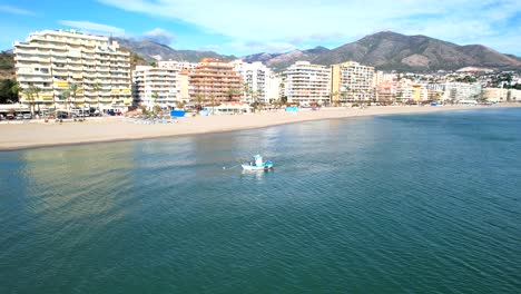 Panorámica-Aérea-A-Través-De-La-Playa-De-Las-Colinas-De-Fuengirola-Con-Un-Pequeño-Remolcador