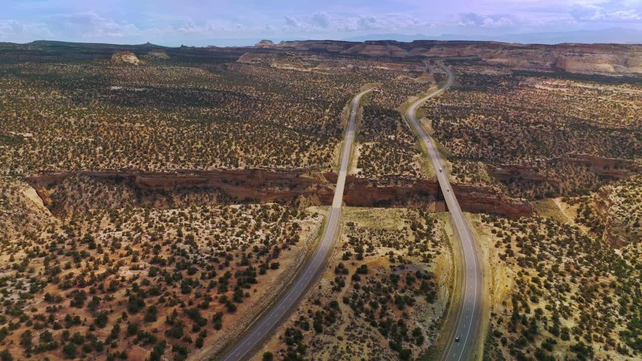 Two long highways passing through the deserted land with little green bushes. Drone approaching the huge crack in the desert with bridges connecting the roads.