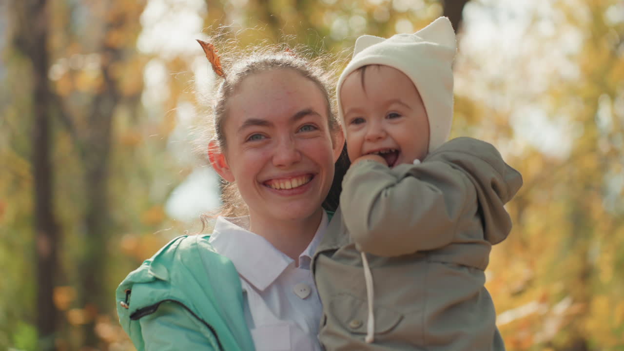 Heller Hain, Bezugsperson hält Baby eng, spielerisches Knabbern und gemeinsames Lachen, schützende Umarmung, authentisches Porträt, Sonnenlicht filtert durch Bäume, zärtliche Interaktion, warmes Familiengefühl