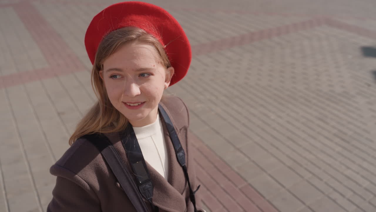 Элегантная городская прогулка. Женщина в красном гуляет по городу. Женщина в ярком наряде исследует городские улицы. Молодая женщина в красном берете и винтажном пальто прогуливается по солнечной городской площади.