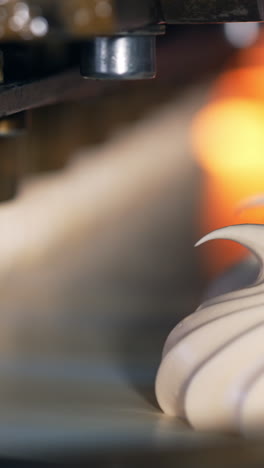 whipped white vanilla cream comes out off a metal nozzle. freshly squeezed marshmallows on the conveyor belt. close up. vertical video