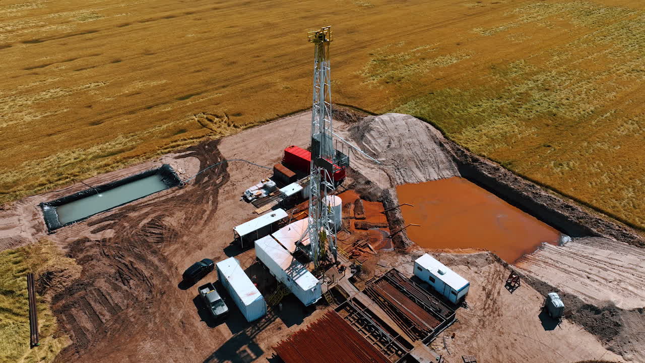 Flying around the derrick in the center of gas drilling site. Cars, wagons and swimming pool surround the rig.