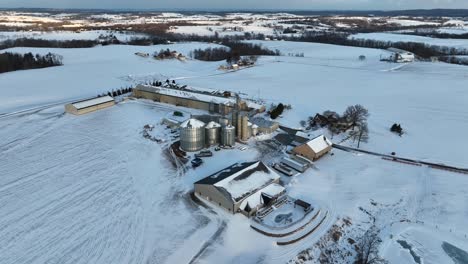 wide aerial view of midwest grain farm and bins covered in winter snow