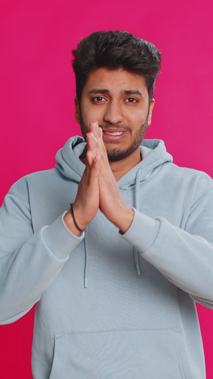 Indian young man pleading begging hands together praying asking for help desperate hopeful indoors