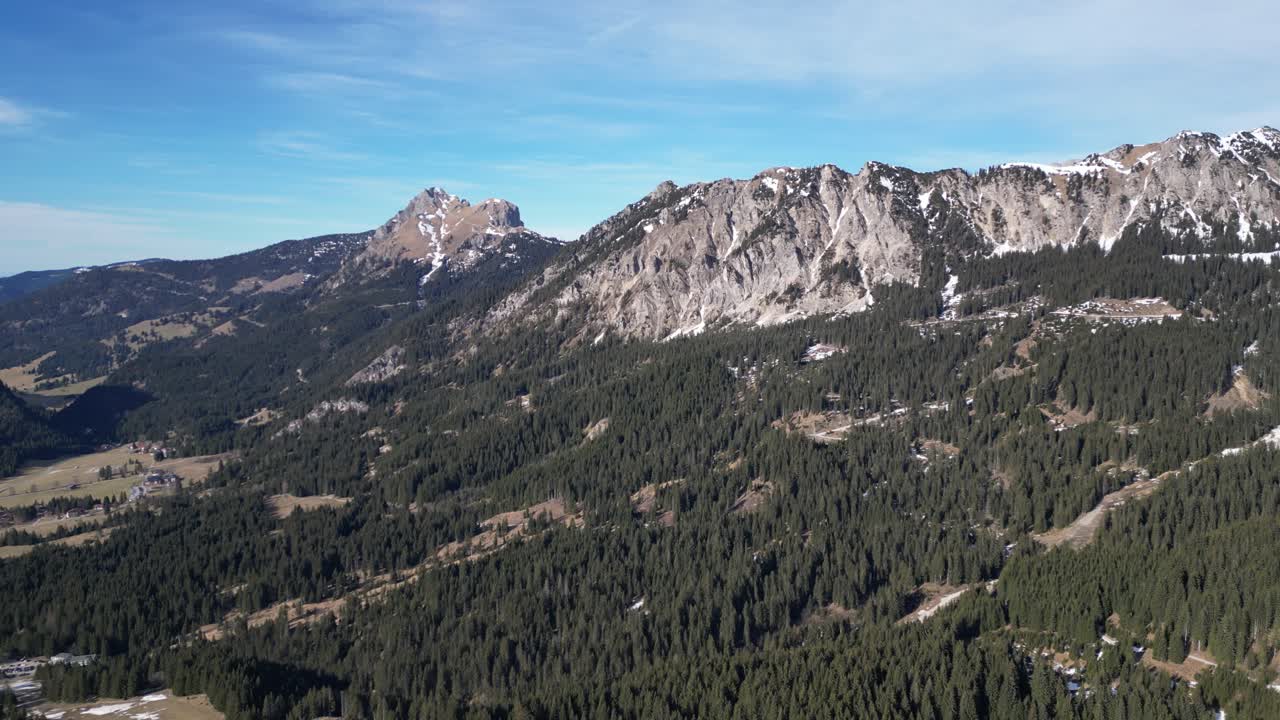 de pie alto contra el cielo azul, la cordillera de tirol tannheimer tal, suiza, adornada con bosques que se extienden hasta el valle de abajo, mostrando el encanto natural del paisaje suizo