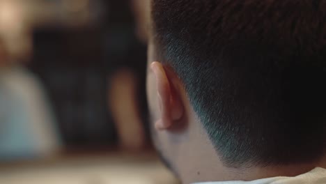 young man sits in barber shop in frame - trimmed hairstyle close-up