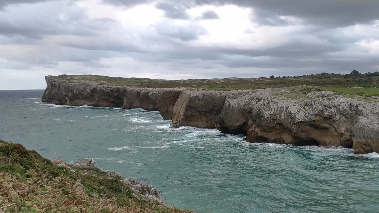 Steep cliffs meet the ocean under cloudy skies at Guadamia cliffs in Asturias